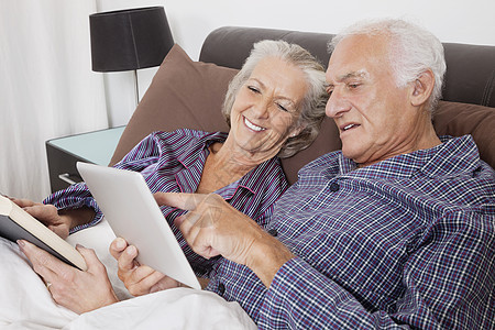 幸福的老年情侣在房间里睡觉时使用数字平板电脑图片