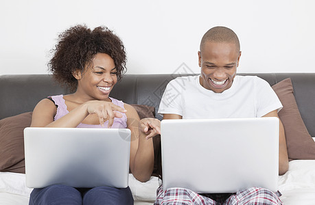 床上使用笔记本电脑的年轻非裔美国夫妇图片