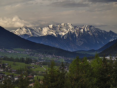 春山乡村景观 俯瞰奥地利因斯布鲁克附近的山谷 那里有 Neder 村 绿色草地 森林 白雪覆盖的阿尔卑斯山峰 夜间戏剧性的云彩和图片