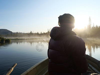 在瑞典拉普兰大自然中美丽的阳光明媚的晨雾中 渔夫在湖划艇 山 白桦树 云杉林 蓝天和背光橙子薄雾爬坡风景垂钓者阴霾男人派对小时旅图片