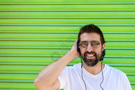 在耳机里吹奏有色背景的音乐 酷酷潮流有趣的胡子男幸福男性胡子绿色服装成人潮人晴天胡须闲暇图片