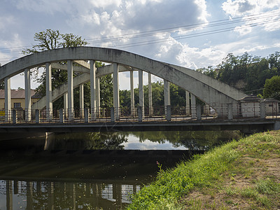 横跨杰泽拉河的老旧弧桥造水泥和金属 在树木和村庄夏季风景上观望图片