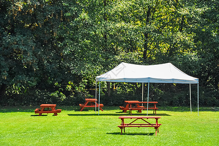 公园绿草坪上有红色野餐桌和白色帐篷的休息区民众草地旅游林地娱乐木头树木桌子享受家具图片