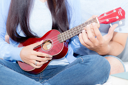 年轻的亚裔夫妇玩着四轮式的游戏男朋友歌曲弦琴房间女朋友长椅浪漫微笑卧室音乐图片