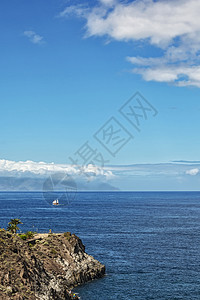 海景 一艘载有白帆的帆船漂浮在岩石海岸上图片