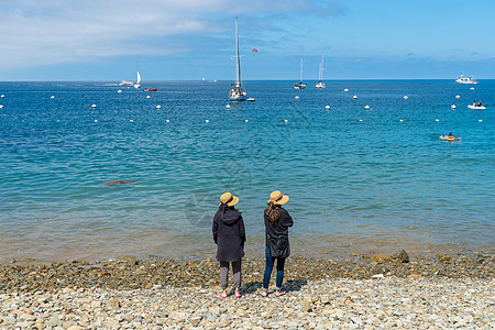 两位女士在岩石海滩上 看着海景和地平线图片
