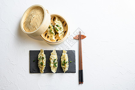 蒸饺子或日本饺子 传统木蒸笼中的饺子小吃和白色纹理石背景上的黑色石板 用于文本的顶视图空间图片