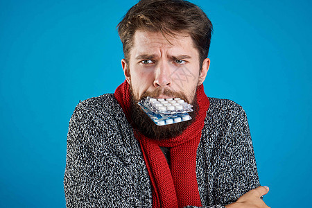 一个口服有药片的男人 手握着牙印 身体健康问题 衣着红围巾鼻子药品疾病疼痛发烧组织流感胶囊蓝色感染背景图片