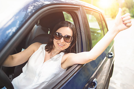 身戴太阳镜的聪明中年成年妇女把手伸出车窗 举起拇指 笑着看女人开车开汽车运输驾驶司机幸福乐趣女士训练旅行成人女孩图片