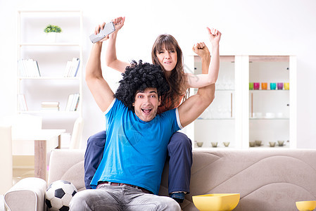 年轻男人在家和妻子一起看橄榄球支持者庆典运动胜利假发幸福观众快乐尖叫游戏图片