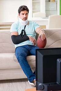 在电视上观看美式足球比赛时 脖子和手臂受伤的男子卫生沙发保健屏幕束缚药品骨科保险疼痛创伤图片