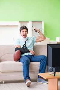 在电视上观看美式足球比赛时 脖子和手臂受伤的男子运动疼痛支持者事故卫生鞭打橄榄球颈椎病支撑沙发图片