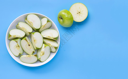 蓝色背景的白色盘子上的新鲜绿苹果切片图片