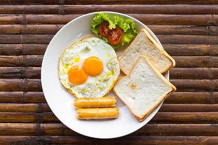 炒鸡蛋 香肠 新鲜番茄 加绿色沙拉和白盘烤面包 放在棕竹桌上 美国早餐 顶级风景图片