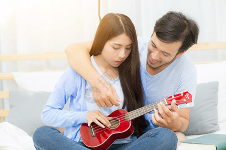 年轻的亚裔夫妇玩着四轮式的游戏女朋友男人微笑唱歌乐器喜悦卧室房间青少年浪漫图片