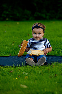 有个漂亮的小女婴坐在花园的草坪上 拿着新鲜的面包包童年绿色生活方式公园食物孩子女孩幸福女性喜悦图片