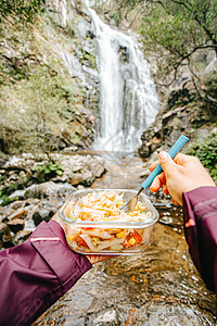 一名女性远足者在瀑布前吃东西的镜头远足烹饪饮食背包旅游男人假期团体冒险帐篷图片