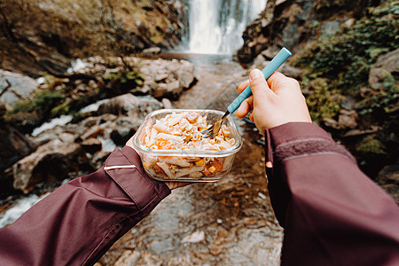 一名女性登山者在瀑布前吃东西的镜头食物木头塑料远足瓶子男人饮食荒野观光团体图片