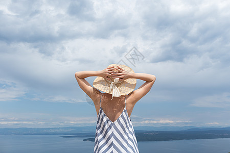 身穿条纹夏季服装和草帽的年轻女子站在野花开花丛露出 放轻松而美观亚得里亚海自然的近视中 克罗地亚晴天天空阳光喜悦女士幸福蓝色裙子图片