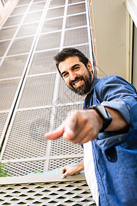 长胡子笑脸的男人靠在墙上 用手指指着你生活成人倾斜企业家胡须城市快乐休闲装相机男性图片