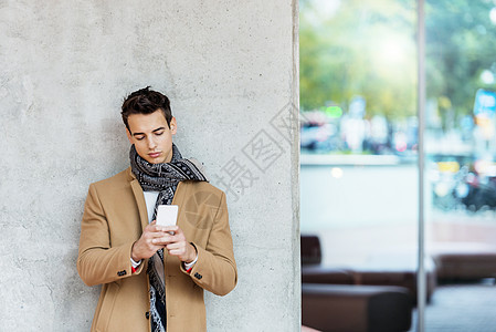 在户外使用移动电话时 身着牛仔服 靠在墙壁上倾斜的时装年轻男子的前视线男人牛仔布牛仔裤外套年轻人围巾街道衣服男性手机图片