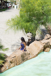 在水池旁边的岩石上坐着 一个美丽的年轻 神秘女性的视线前方图片