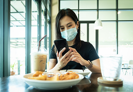 一位亚洲美女必须戴蓝面罩 为准备面具早餐电话食物油炸咖啡头发椅子咖啡店牛奶图片