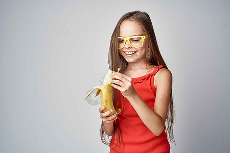 身戴眼镜的小女孩和手上拿着香蕉的红礼服 轻光背景女士冒充背包快乐魅力帽子眼镜微笑女孩公主图片
