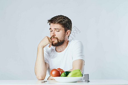 坐在桌子上健康地吃蔬菜的男子 白T恤饮食浅底背景沙拉食物幸福男人男性药品水果橙子微笑乐趣图片