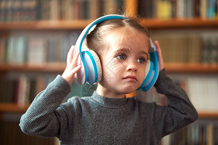 穿着白色大耳机的白人可爱小女孩 在内地用书架的背景来听音乐 笑声乐趣幸福童年女孩立体声女性娱乐孩子金发微笑图片