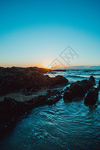 蓝色和橙色的日落在海滩岩石上海浪旅行海岸线小径海岸季节海景阳光旅游天空图片