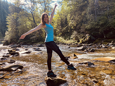 年轻女子在山流的石头上做瑜伽锻炼图片