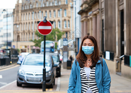 身戴面罩的亚裔妇女在城市周围走动背景图片