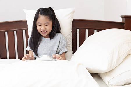 亚裔小女孩笑着手握手 玩平板电脑毯子女性触摸屏互联网手指枕头教育孩子时间房间图片