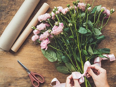带有玫瑰 剪刀 手纸和p的木制桌子顶端视图工作作品粉色女士植物花束牛皮纸包装花店丝带图片