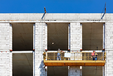 建筑工人爬上正在建设中的建筑物立面上的支架图片