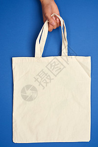 女性手握着一个空的米色织物袋 用在A上的把手边购物织物市场白色回收亚麻零售蓝色帆布小样图片