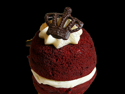 一个红色天鹅绒蛋糕的紧贴 上面有一个巧克力皇冠 隔绝在黑色背景上图片