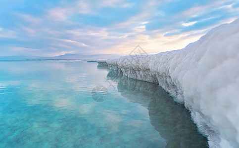 完全被结晶盐覆盖的沙子看起来像死海岸边的冰或雪 近处碧蓝的海水 清晨的阳光照耀着天空 — 以色列 Ein Bokek 海滩的典型图片