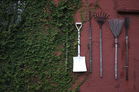 红色水泥墙上挂着的园艺工具草地木头工作乡村植物花园农业农场团体金属图片
