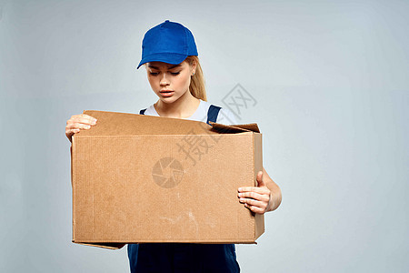 一名身穿工作制服 手里拿着一个盒子的女性 在送货服务的灯光背景下女孩工作室女士工人商业纸板导游成人微笑纸盒图片
