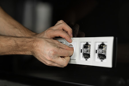 特写电工的手 不带任何工具和手套 在黑玻璃墙上拆卸白色电源插口 (单位 美元)图片