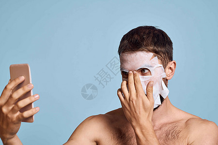 一个脸上有清洗面具的人 用蓝色背景的镜子在镜子里对自己进行检查 照片来自剃须温泉卫生男人浴室眼睛身体奶油男生头发图片