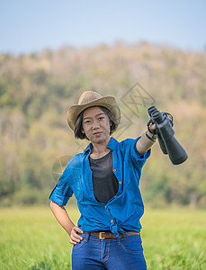 妇女戴帽子 在草地佩戴望远镜冒险农村监视森林野生动物活动女士闲暇间谍天空图片