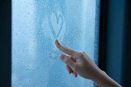 女性手绘在雨中雾蒙蒙的窗户上画一颗心 玻璃中的水滴 浪漫的概念宏观气泡蓝色手指蒸汽绘画女孩天气雨滴水分背景图片