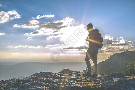 日落时背着背包站在悬崖上的人图片