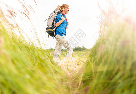 年轻女孩带着背包在草地上行走游客旅游闲暇场地远足者小路蓝色金发女郎假期场景图片