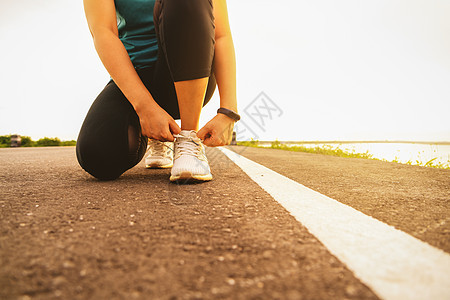 在日落湖上跪和系鞋带的女运动员运动装赛跑者跑步阳光公园运动鞋运动太阳成人女士图片