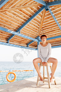 红色短头发剪红的年轻女子坐在木头码头上活命阳光沿海旅游青春头发假期椅子天空海滩地方图片