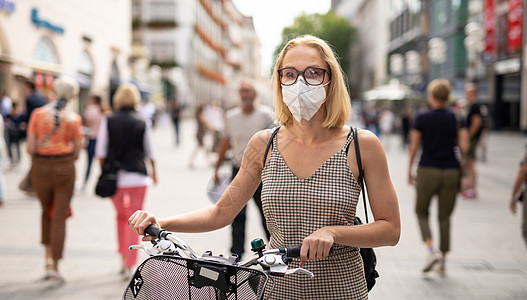 妇女用自行车在行人城市街道上走路 在公共场合戴医疗面罩 以防止科罗纳病毒传播 在贪食流行期间是新常态运输症状面具疾病手术男人责任图片